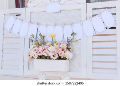 White wooden flower box with cream, pink and yellow eustomas and a garland of seating chart on window frame
