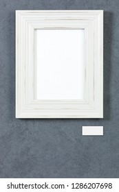 White Wooden Frame On Grey Painted Wall, Picture Area Isolated With Clipping Path. Blank Caption Tag And Copy Space Below