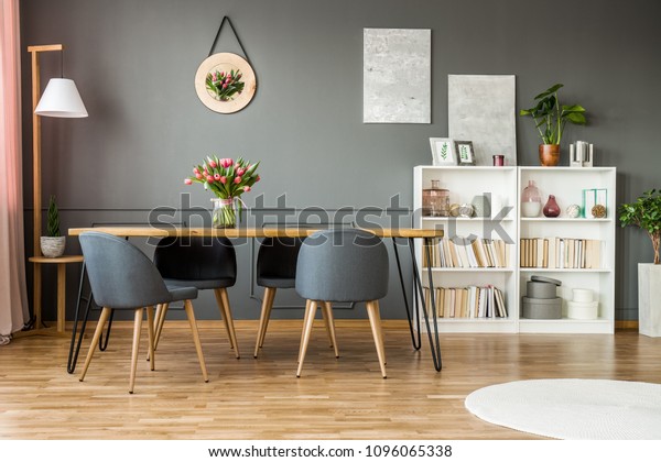 White\
wooden rack with books, decor and fresh plants standing in grey\
dining room interior with flowers on hairpin\
table