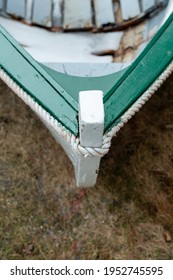 A white wooden rodney boat with bright green edging and a grey interior sits on the ground near the ocean.The bow of the dory is in the foreground. A traditional Newfoundland fishing boat newly built.