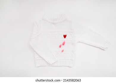 White woolen sweater with a red heart shaped pin on white background top view. Love, romance, fashion concept. Flat lay, copy space