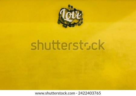 the white word “love” with green leaf is attached to the yellow wall with copy space at the bottom of the frame, valentine concept