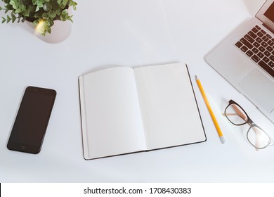 White work table with notes, smartphone and laptop