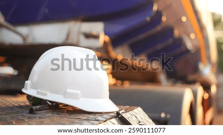 A white worker protective hardhat or helmet is placed on truck or machine part. Safety equipment PPE at unsafety workplace industrial, object photo.