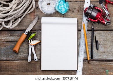 White Writing-book With Fishing Tackles And Design Tools On Wooden Board. For Mockup, Print, Design.