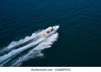 White yacht fast moving on clear water aerial side view. A large white boat at high speed on the water leaves a white trail, top view.