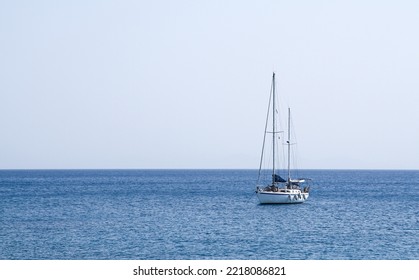 A White Yacht With Lowered Sails On Blue Water In The Sea. Vacation On A Yacht In Summer. A Small Boat Is Anchored In The Port.A Ship In The Open Ocean.