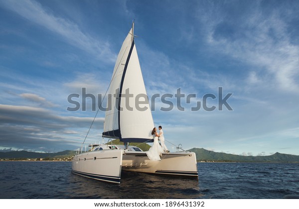 white yacht with sail set goes along\
the island on a hot day. blue sea, blue sky. on board a young\
couple in love. the bride and groom. wedding boat\
trip