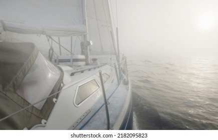 White yacht sailing in the Baltic sea. Thick fog. Sunrise. Sweden. Close-up view from the deck to the bow and sails. Morning sun, glowing clouds. Sport, recreation, leisure activity, cruise, regatta - Powered by Shutterstock