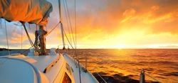 White Yacht Sailing In An Open Sea At Sunset. A View From The Deck To The Bow, Mast, Sails. Epic Cloudscape. Dramatic Sky With Glowing Golden Clouds After The Storm. Racing, Sport, Leisure Activity