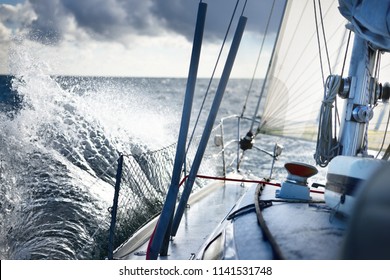 White yacht sailing in an open sea. View from the deck to the bow. Rough weather, storm, dramatic sky, dark clouds, waves, water splashes. Transportation, travel, sport, recreation, leisure activity