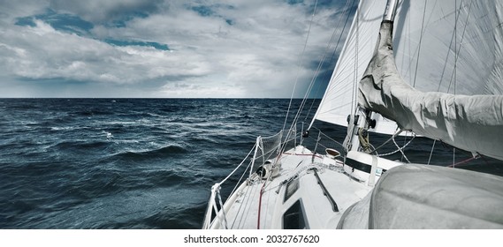 White Yacht Sailing In An Open Sea During The Storm. View From The Deck To The Bow. Rough Weather, Dramatic Sky, Dark Clouds, Waves, Water Splashes. Transportation, Travel, Sport, Leisure Activity