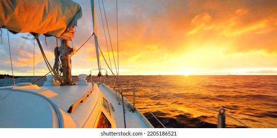 White yacht sailing in an open sea at sunset. A view from the deck to the bow, mast, sails. Epic cloudscape. Dramatic sky with glowing golden clouds after the storm. Racing, sport, leisure activity - Powered by Shutterstock