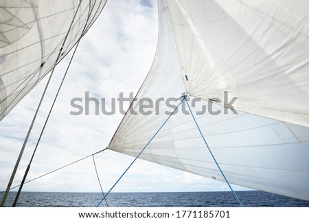 White yacht sails against clear blue sky with lots of clouds. Sailing in an open Mediterranean sea. Idyllic cloudscape. Summer vacations, leisure activity, sport and recreation, private wessel