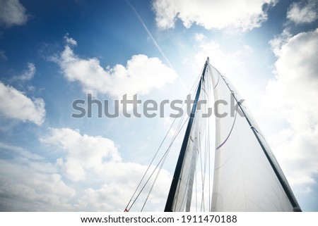 White yacht sails against clear blue sky with lots of clouds. Sailing in an open Mediterranean sea. Idyllic cloudscape. Summer vacations, leisure activity, sport and recreation, private wessel