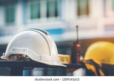 White And Yellow Helmet  With Construction Water,gloves And Radio That Are Placed On Steel House Fence.