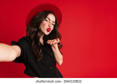 White young woman taking selfie photo while blowing air kiss isolated over red background - Powered by Shutterstock
