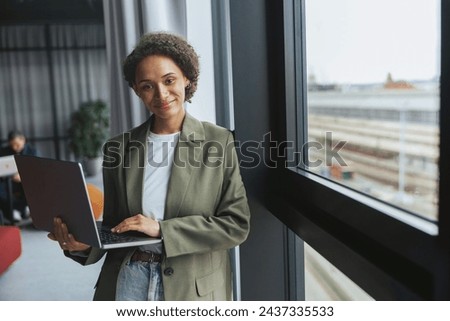 A whitecollar worker in formal wear holds a laptop by a window at a building