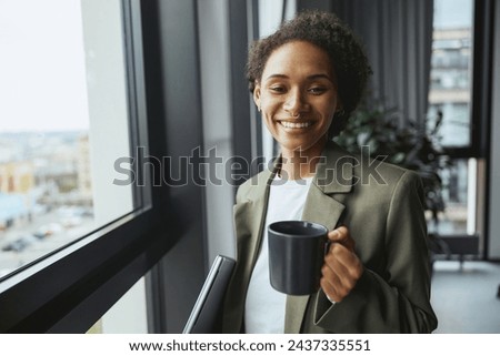 A whitecollar worker gazes out a window with a cup of coffee, smiling