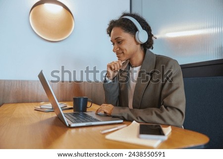 A whitecollar worker with headphones is using a laptop at a desk