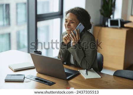 A whitecollar worker is on the phone at a desk with a laptop and window