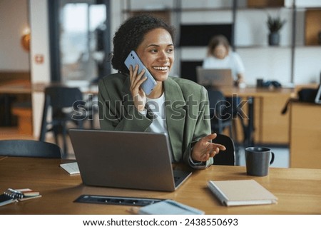 A whitecollar worker sits at a desk with a laptop and talks on a cell phone in nice modern coworking office
