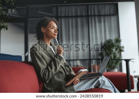 A whitecollar worker is sitting in a room with a laptop and a pen in her mouth