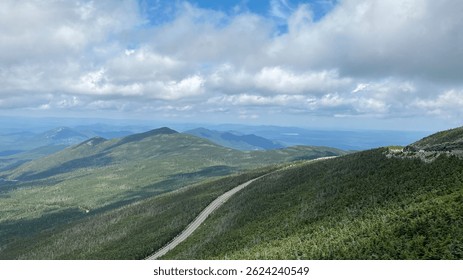 Whiteface Mountain, New York, USA. Scenic panoramic view of a forest-covered mountain range in the Adirondacks, with a winding road and layered blue ridges under a cloudy sky.