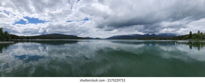 Whitefish Lake in Flathead County, Montana under dramatic summer cloudscape reflected in calm water of lake.