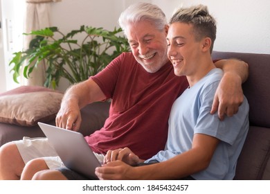 White-haired Grandfather And Teenage Grandson Enjoying Surfing The Net With Laptop. Young And Old Together Share Modernity And Technologies