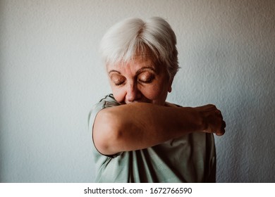 
White-haired, middle-aged woman with coronavirus symptoms coughing correctly on her elbow. Global health crisis. Pandemia - Powered by Shutterstock