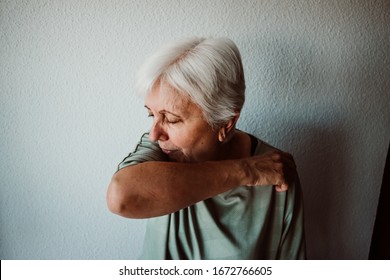 
White-haired, middle-aged woman with coronavirus symptoms coughing correctly on her elbow. Global health crisis. Pandemia - Powered by Shutterstock