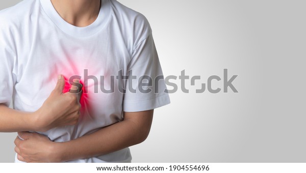 A\
white-robed Asian woman showed chest pain by putting her hand on\
the center of her chest. health issues, an empty space on the\
right-hand side of the image to insert\
text.