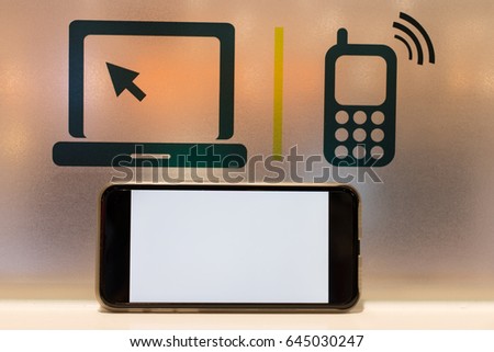 A white-screen smart phone on a wooden table. Computer and mobile device icons on the orange-light ground glass background