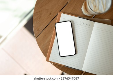 A white-screen smartphone mockup on an opened book on a wooden table in a cosy minimalist coffee shop. workspace top view - Powered by Shutterstock