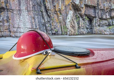 Whitewater Kayaking Helmet On A Kayak Deck Against River Rapid And Cliff