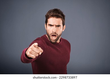 Who do you think you are. Studio shot of a handsome young man pointing a finger in anger against a gray background.