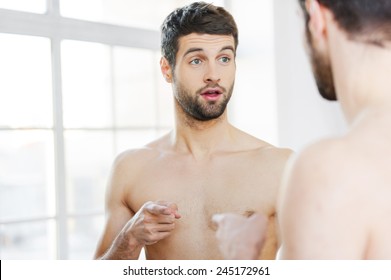 Who Am I? Frustrated Young Shirtless Man Pointing Himself While Standing Against A Mirror 