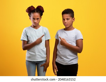 Who Is Guilty. Angry Black Brother And Sister Having Fight, Afro-american Boy And Girl Pointing At Each Other, Yellow Studio Background. Siblings Relationships, Kids Quarrels Concept