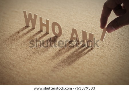 WHO AM I wood word on compressed or corkboard with human's finger at I letter.