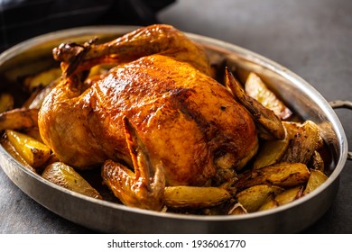 Whole baked golden crispy chicken in a pan cooked with potatoes.