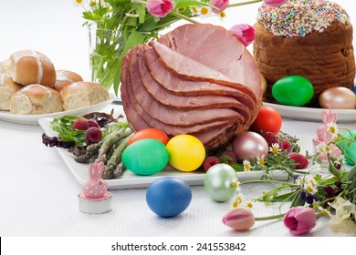 Whole baked honey sliced ham with fresh raspberry, asparagus, dyed Ester eggs, Easter cake, and cross buns. Spring flowers. 