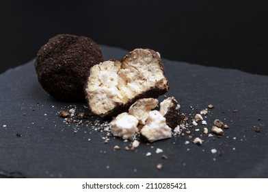 A whole and broken ball of Belper Knoll cheese lies on a black slate board. Hard Swiss cheese in the form of small balls in a sprinkle of black pepper. side view.