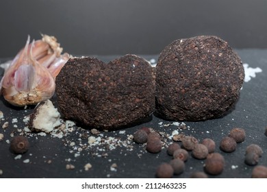 whole and broken ball of Belper Knoll cheese, black pepper, salt and garlic cloves lying on a black slate. Hard Swiss cheese in the form of small balls, sprinkled with black pepper, close-up.