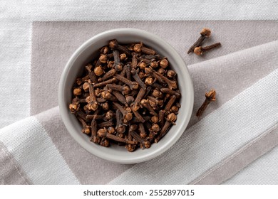 Brotes de clavo enteros en un tazón sobre fondo textil gris. Macro de especias orgánicas secas de clavo de olor en un Pequeño cuenco gris. Cocina, medicina herbal y concepto de especias. Vista superior.