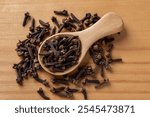 Whole cloves spice in a spoon over wooden background. Wooden spoon full of dry clove buds macro. Spice for cooking and herbal medicine concept. Top view.