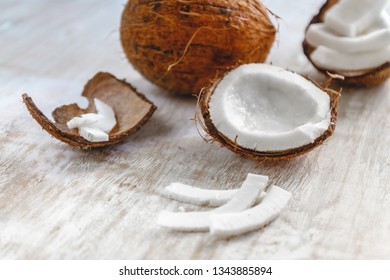 Whole Coconut And Cut Into Chunks And Chips On A Light White Wooden Background.