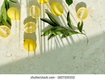 Whole And Cut Lemons And Leaves On A Stone Surface Under Shadow Of Palm Tree Leaf. Top View