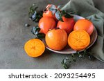 Whole and cut persimmon fruit with water drops and green leaves on green concrete background.