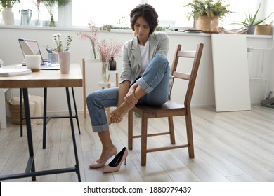 Whole day on stilettos. Tired young female florist decorator sitting on chair at work table taking off high heel shoe. Fatigued lady manager of craft store flower shop massaging bare foot feeling pain - Powered by Shutterstock